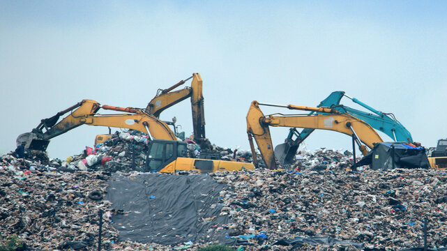 Heavy excavators clearing massive piles of debris and garbage in the aftermath of a severe flood disaster during a rescue operation.