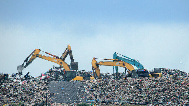 Industrial backhoes clearing a mountain of trash and destroyed property during a post-flood recovery and search operation.