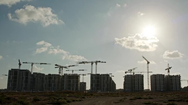 Silhouette Of Multiple Tower Cranes Operating On Large Construction Site Under Cloudy Sky During Sunset Time Lapse