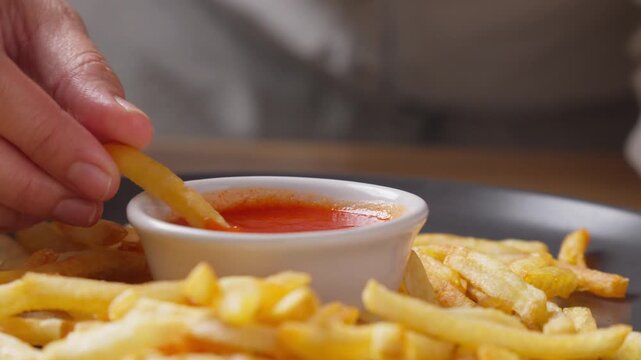 Person dipping French fries into a chili hot sauce, close up shoot