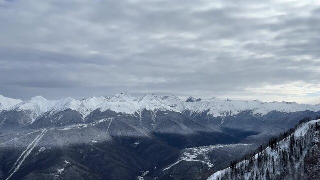Snow-covered mountains under a cloudy sky. The landscape features rugged peaks and a valley, showcasing winter scenery and natural beauty.