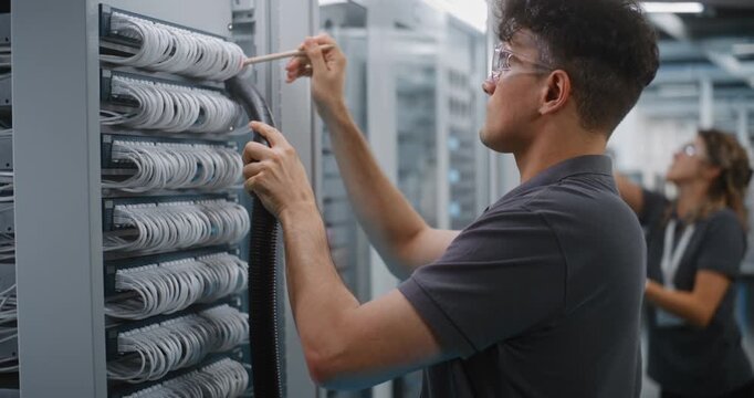 Male Network Technician Uses Soft Brush and Vacuum Nozzle to Clean Dust Off Ethernet Patch Panel Cables Inside Open Server Rack. Hardware Cleaning Prevents Connection Errors and Hardware Failure.