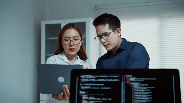 Asian team of developers working on software code, talking and collaborating together in a modern office at night