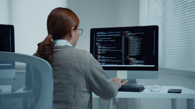 Professional female programmer coding on computer in a modern it company office while debugging software code