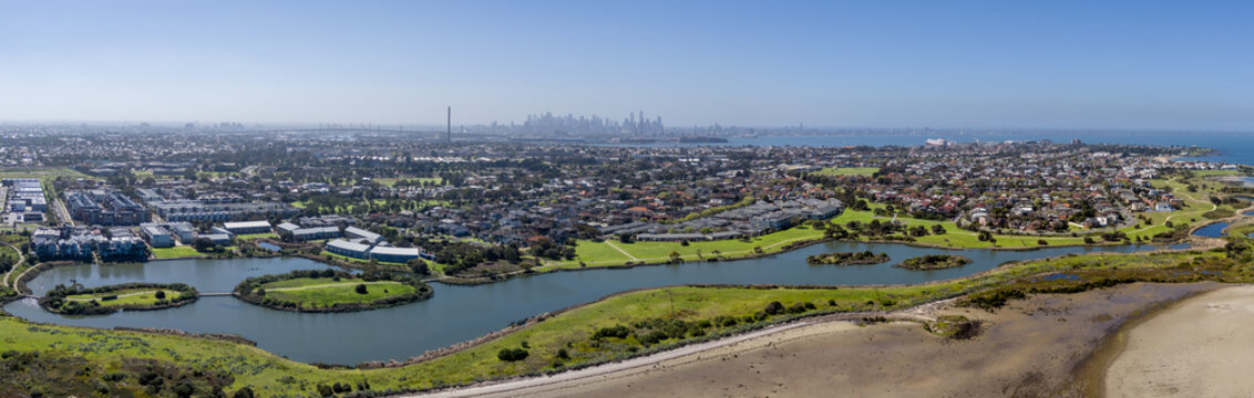 Wide aerial panorama of Jawbone Flora and Fauna Reserve wetlands and marine sanctuary in Williamstown, with residential housing, coastal foreshore, and Melbourne city skyline, Australia