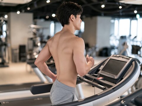 スポーツジムで上半身を露出しランニングマシンで汗を流す筋肉質の男性