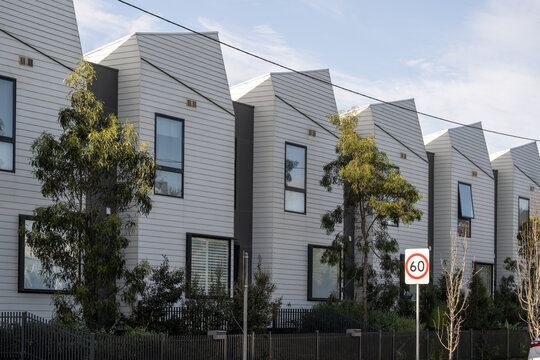 Row of modern architecturally designed townhouses with angular rooflines and cladding facades, Australian native trees, and a 60km/h speed sign, Melbourne, Victoria, Australia. Concepts of real estate