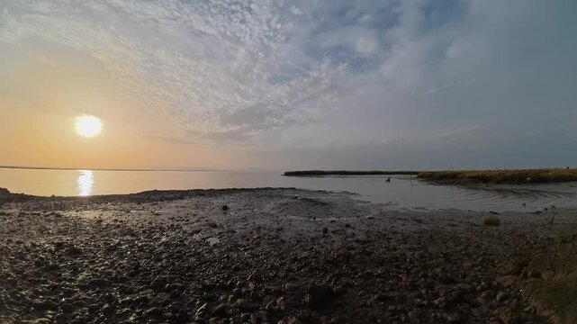 Beautiful timelapse of the rising tide in Sado estuary, Setubal, as the golden sunset sky reflects on tranquil water, rocky shore transitions into calm tidal pools, and vibrant evening clouds appear.