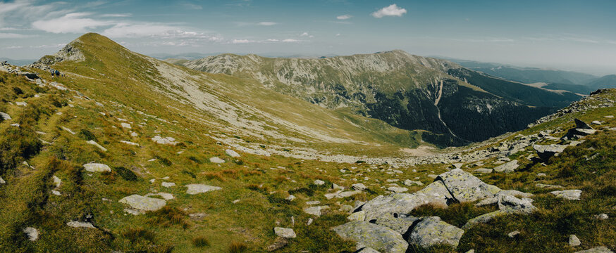 Panoramic view of rugged alpine landscape with scattered rocks on grassy slopes and high mountain ridges.