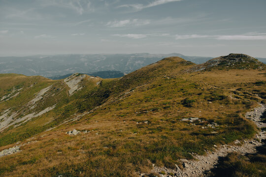 Scenic view of grassy alpine ridges and mountain slopes under a summer sky in Parang, Romania.