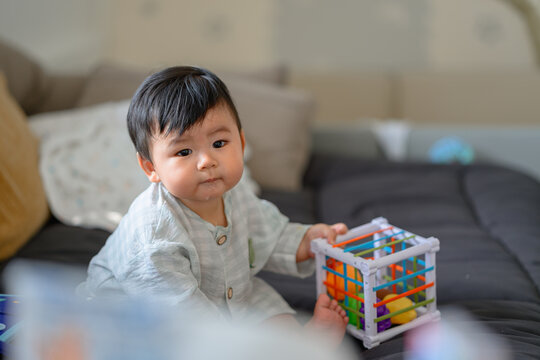 Cute Asian baby boy playing with colorful sensory shape sorter toy at home