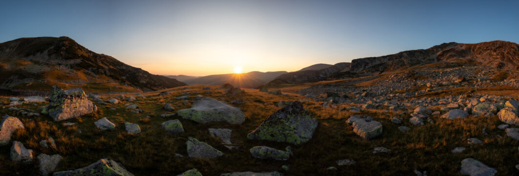 Panoramic picture of dramatic golden sunrise illuminating rocky peaks and scattered boulders in the Parang mountains.