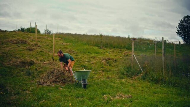 Man raking grass in a rural landscape, working outdoors among open grassy fields and countryside surroundings