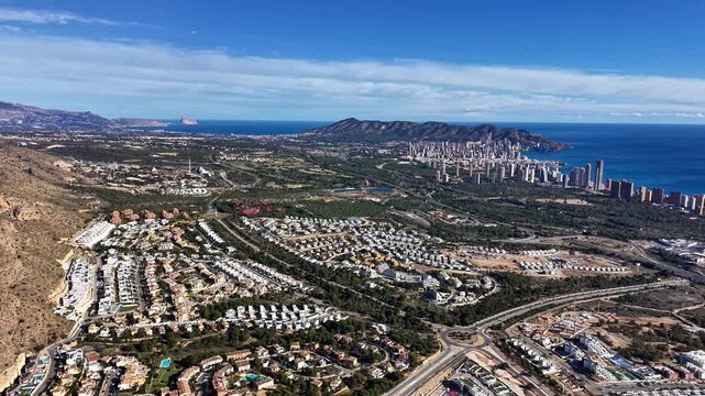 Aerial Resort Coastline With City Skyline Sunlit Drone Glide Revealing Gated Villas, Pools, Winding Roads