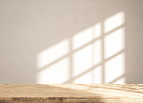 Empty tabletop stands beneath sunlit backdrop. Window shaped light patterns brighten beige wall and wood grain, forming serene interior scene with natural texture and generous copy space.