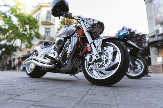 Custom motorcycle stands parked on stone pavement with chrome details and graphic paint. Bike looks powerful and polished, while helmet on handlebar adds ready to ride attitude in city setting.