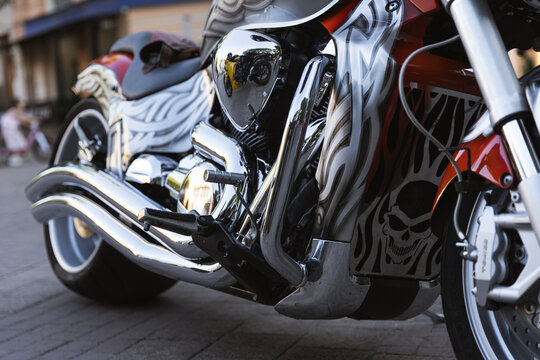 Custom motorcycle rests on pavement with chrome engine and skull artwork. Motorcycle styling feels bold and rebellious, with polished metal reflecting surroundings in close low angle view.