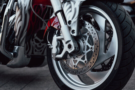 Custom styled motorcycle front wheel dominates frame with sharp detail. Brake disc, fork and tire are shown beside skull graphic bodywork, creating dramatic custom look with sleek metal finish.
