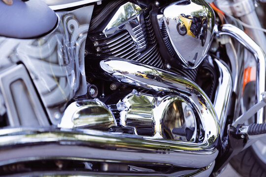 Motorcycle engine detail gleams in close up, with chrome bodywork reflecting another yellow bike nearby. Motorcycle detail highlights polished mechanical surfaces and parked outdoor display.