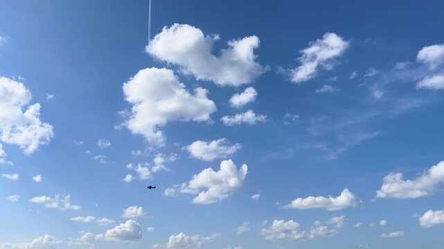Small propeller airplane flies beneath scattered white clouds in a bright blue sky