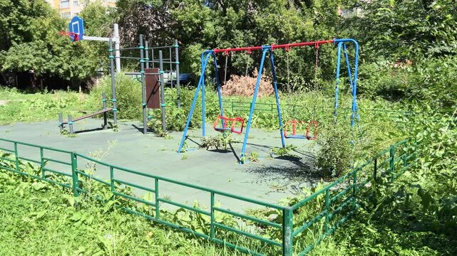 Empty colorful swings swinging in a green neighborhood playground on a sunny summer day