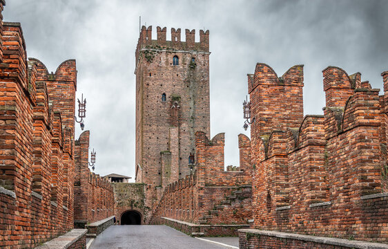 The iconic red brick fortified medieval Castelvecchio Bridge with swallowtail merlons over the Adige River leading towards the central watchtower of the Scaliger Castle in Verona, Veneto, Italy under 