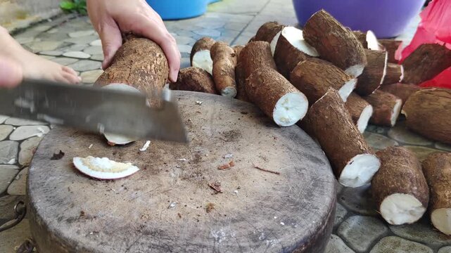 A hand cutting fresh cassava (yuca) on a wooden cutting board in preparation for a traditional dish.