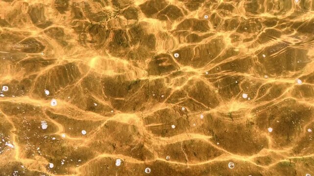 Golden sunlight ripples across clear shallow beach water above sandy bottom