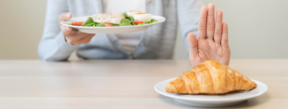 Close up of a woman hand gesturing stop to refuse eating croissant for her weight loss diet program in a bright clean dining room