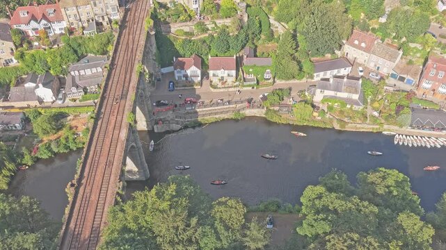 Knaresborough Viaduct and its double-track railway corridor cross the River Nidd beside riverside houses, boats and wooded banks in Knaresborough, North Yorkshire, England, United Kingdom, parallax dr