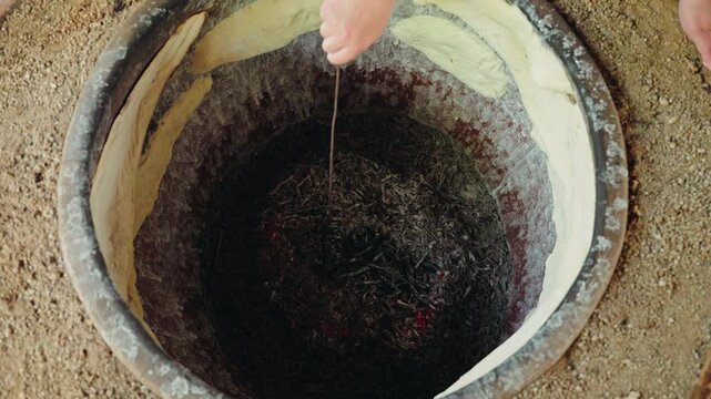 Looking down into a traditional Georgian tone oven, red embers glow at the bottom while lavash dough bakes on the clay wall.