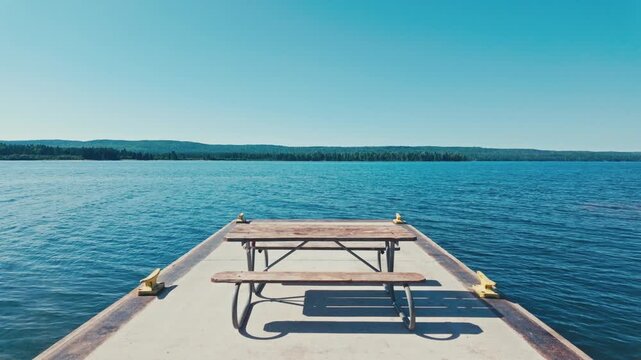 A picnic table at the end of a large pier surrounded by the waters of Lake Superior and the distant tree lines of Isle Royale National Park.