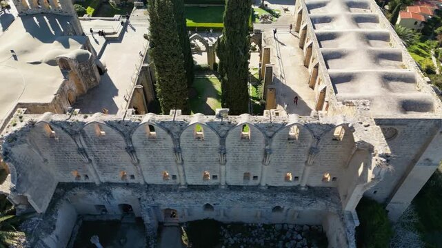 Aerial drone footage of Bellapais Abbey showing the inner courtyard, surrounding stone walls, monastery buildings and rooftops of the historic Gothic complex.  North Cyprus