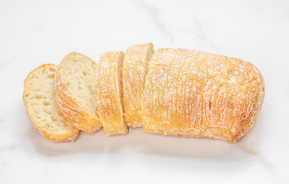 Freshly baked ciabatta bread loaf sliced into pieces on a marble countertop, showcasing the crusty exterior and soft interior texture