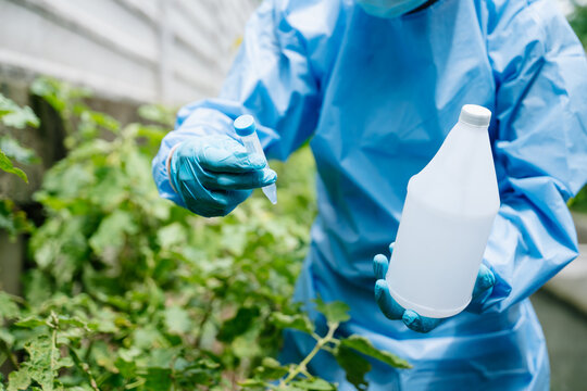 Agronomist in a protective suit holding a test tube and flask in a green garden. Outdoor laboratory research focusing