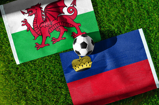 Wales vs. Liechtenstein football match. National flags on green grass with soccer ball in the middle. Football background for international match.