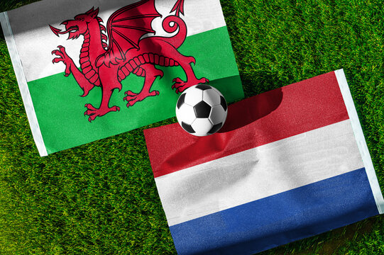 Wales vs. Netherlands football match. National flags on green grass with soccer ball in the middle. Football background for international match.