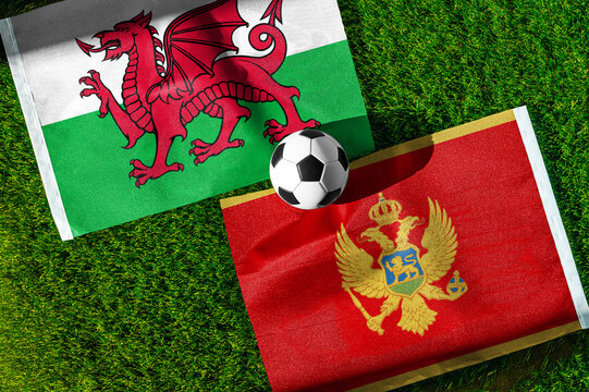 Wales vs. Montenegro football match. National flags on green grass with soccer ball in the middle. Football background for international match.