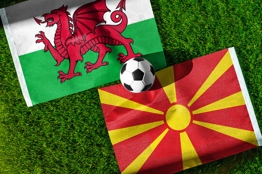 Wales vs. North Macedonia football match. National flags on green grass with soccer ball in the middle. Football background for international match.