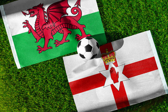 Wales vs. Northern Ireland football match. National flags on green grass with soccer ball in the middle. Football background for international match.
