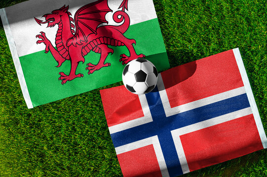Wales vs. Norway football match. National flags on green grass with soccer ball in the middle. Football background for international match.
