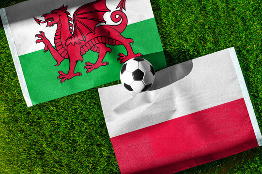 Wales vs. Poland football match. National flags on green grass with soccer ball in the middle. Football background for international match.
