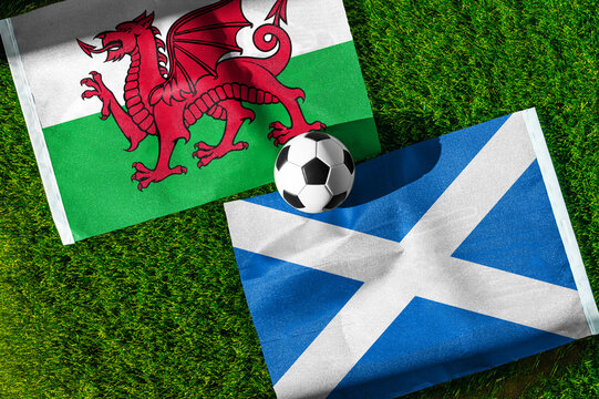 Wales vs. Scotland football match. National flags on green grass with soccer ball in the middle. Football background for international match.