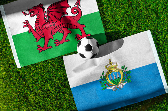Wales vs. San Marino football match. National flags on green grass with soccer ball in the middle. Football background for international match.