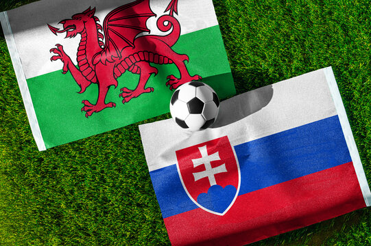 Wales vs. Slovakia football match. National flags on green grass with soccer ball in the middle. Football background for international match.
