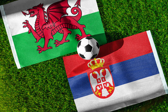 Wales vs. Serbia football match. National flags on green grass with soccer ball in the middle. Football background for international match.