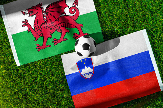 Wales vs. Slovenia football match. National flags on green grass with soccer ball in the middle. Football background for international match.