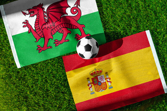 Wales vs. Spain football match. National flags on green grass with soccer ball in the middle. Football background for international match.