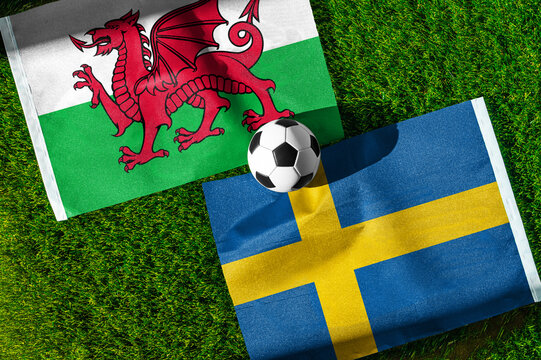 Wales vs. Sweden football match. National flags on green grass with soccer ball in the middle. Football background for international match.