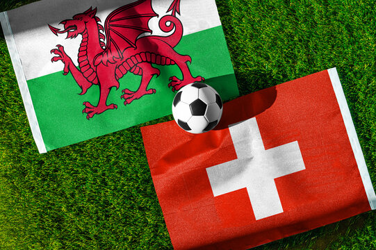 Wales vs. Switzerland football match. National flags on green grass with soccer ball in the middle. Football background for international match.